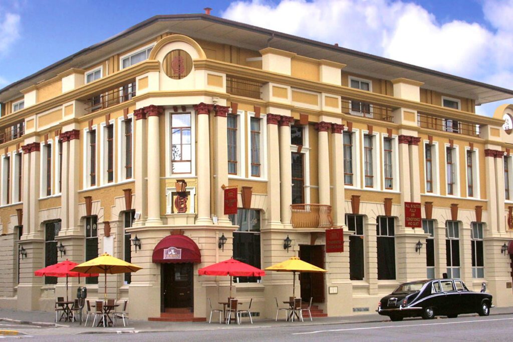 A orange, cream and burgundy art deco building with red and yellow sun umbrellas in the foreground